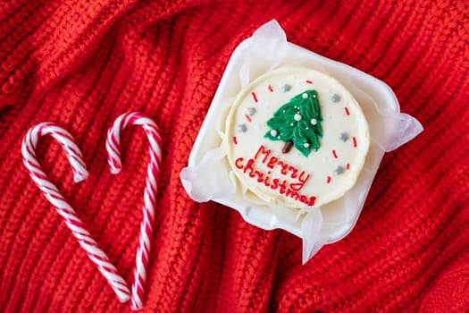 Christmas cupcake with a candy cane heart on a red knitted background. Merry christmas cake inscription.