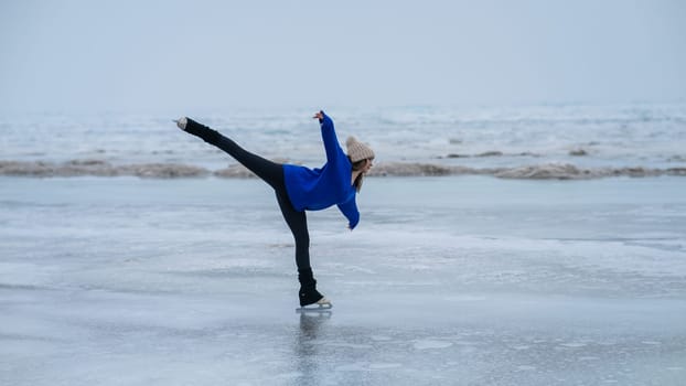 Caucasian woman in a blue sweater is skating on a frozen lake. Figure skater performs a swallow.