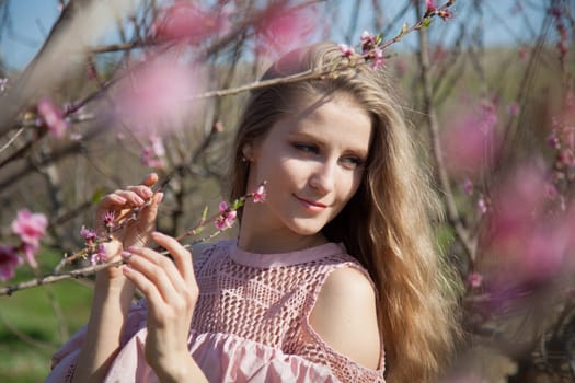 happy blonde woman in pink dress walks through the flowering garden in spring