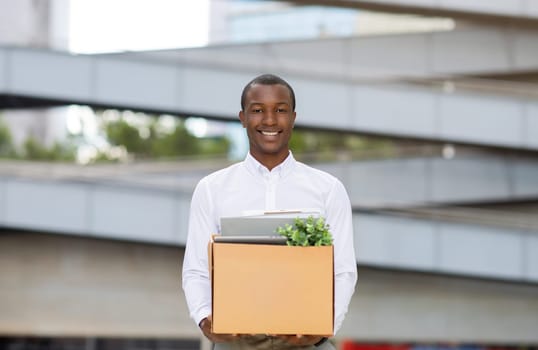 Happy black man in white shirt posing outdoors with box of belongings