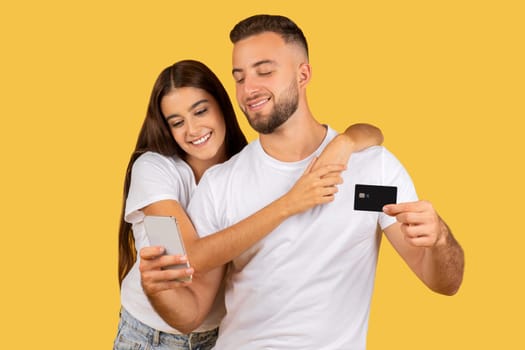 Glad millennial european lady shopaholic hug man in white t-shirts, with credit card and phone