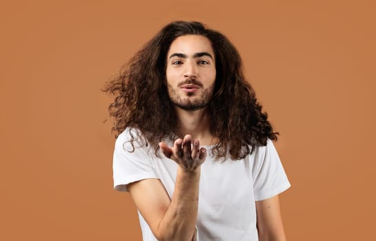 Carefree Arabic Guy With Long Hair Blowing Kiss, Brown Background