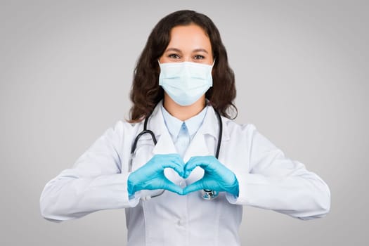 Woman doctor in mask making heart sign with hands