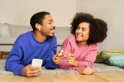 African couple relaxes listening music on phone using earbuds indoor