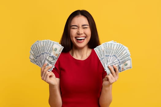 Happy emotional asian woman holding bunch of money banknotes