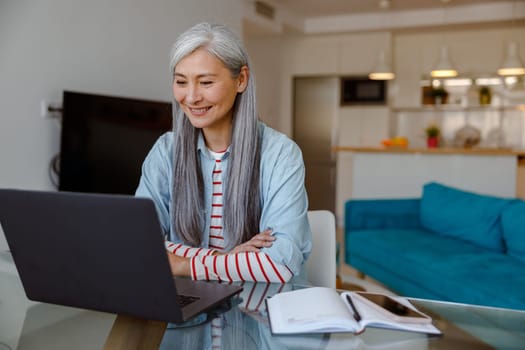 Joyful woman sitting at the table and using laptop at home