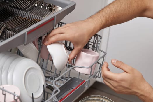 man unloading from open dishwasher machine with clean utensils inside