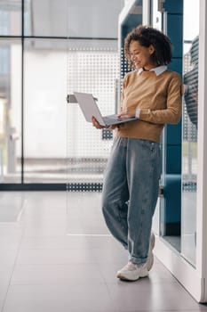 Smiling female freelancer working on laptop while standing on modern coworking background