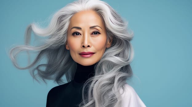 Smiling, elderly, gorgeous Asian woman with gray long hair and perfect skin, on a blue background, banner.