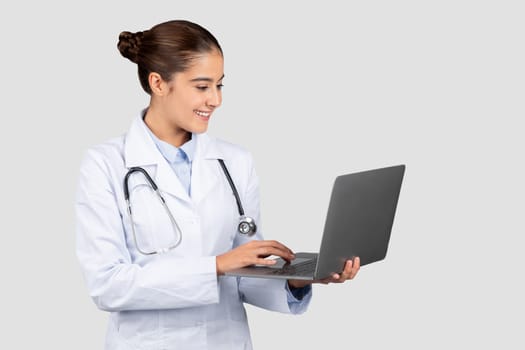 Positive millennial european lady doctor typing on computer, chatting with patient