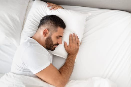 man sleeps in bed hugging pillow for comfort in bedroom