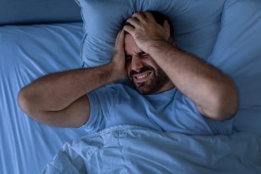 guy suffering from migraine feeling sick at night in bedroom