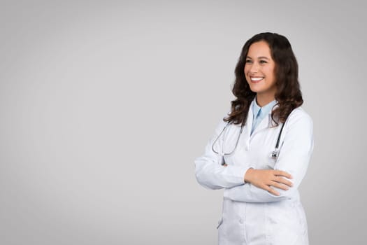 Confident european doctor woman in uniform standing with folded arms looking away at copy space