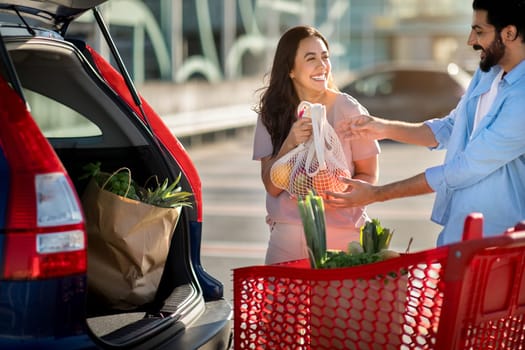 Couple packing groceries into car trunk and laughing