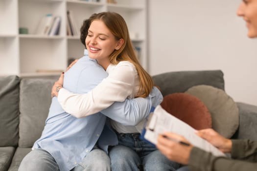 Smiling young couple embraces on sofa after reconciliation at therapy