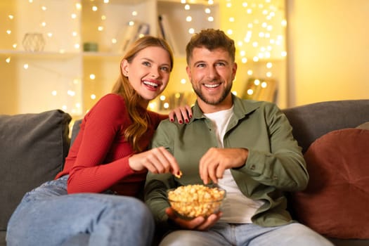 Happy couple sharing popcorn on cozy sofa