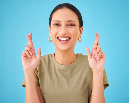 Woman, cross fingers and studio portrait for smile, emoji or sign for hope by blue background. Girl, person and hands for good luck, wish or excited with icon, symbol or faith for results in contest