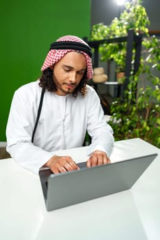 Young Arab man in traditional dress thobe working on computer in office