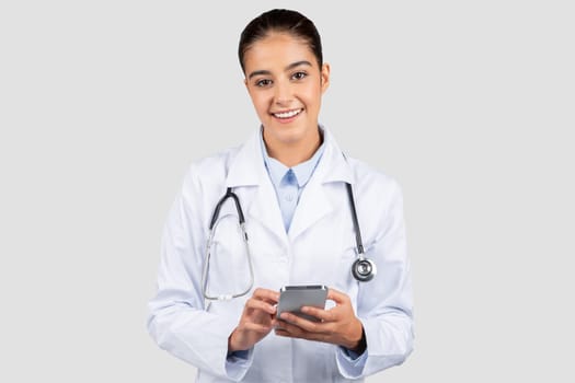 Smiling young caucasian woman professional doctor or intern typing on smartphone, chatting