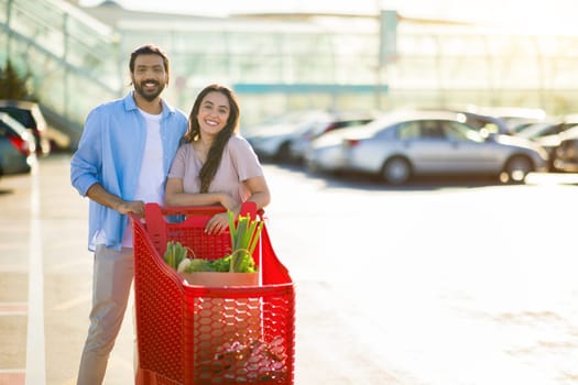 Cheerful arab couple with shopping cart outdoors, free space