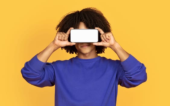 Young black guy covering eyes with blank smartphone