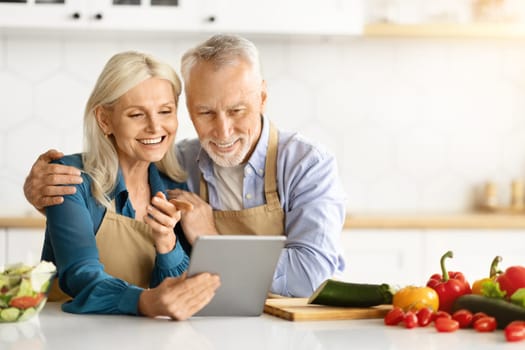 Online Recipe. Happy Senior Couple Using Digital Tablet In Kitchen While Cooking