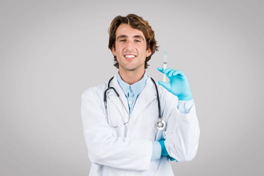 Smiling doctor with syringe ready for vaccination on gray background