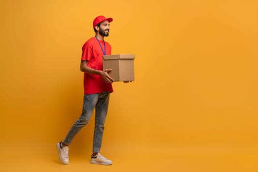 Smiling delivery man in red uniform and cap carrying a cardboard box