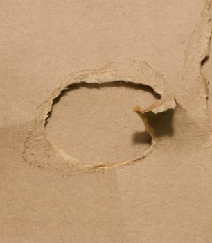 Hole with torn edges in brown cardboard