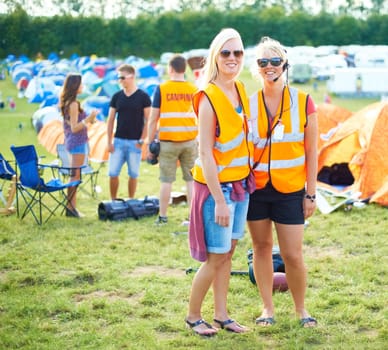 Portrait, sunglasses and event staff at festival for music, party and carnival outdoor in summer. Happy women, girls camping and security team in headset, safety vest or celebration concert in nature.