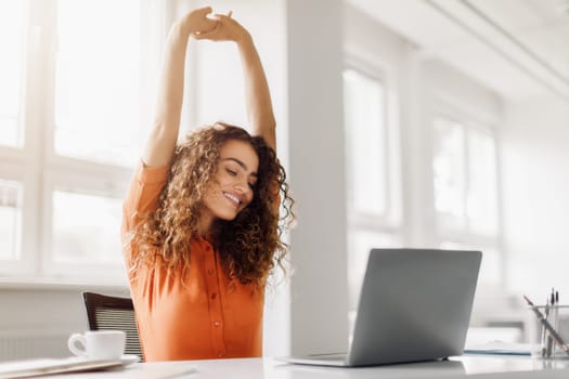 Relaxed woman stretching at her desk with laptop, copy space
