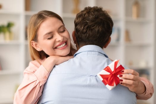Wife Hugging Husband Holding Wrapped Present Box At Home