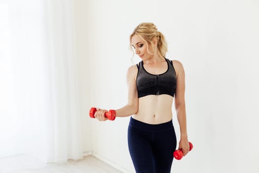 Beautiful blonde woman sports with fitness dumbbells in the hall