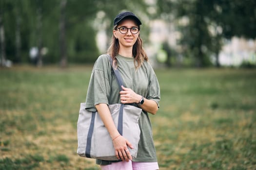 Young woman with glasses holding empty cotton eco bag, mockup design.