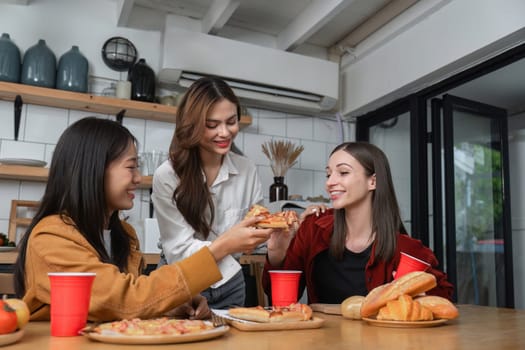 A group of young female friends have a party with pizza on the table and red drink glasses. Talk and live together happy, having fun at home.