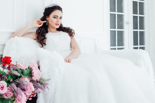bride in a wedding dress and a crown sits in the white hall