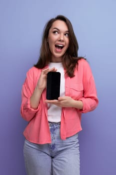 a cute brunette lady with dark hair below her shoulders in a shirt and jeans demonstrates a smartphone screen forward