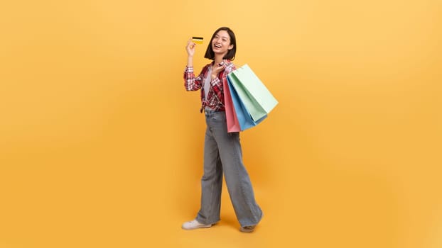 Unlimited shopping concept. Asian lady holding colorful shopper bags and showing credit card, full length, copy space