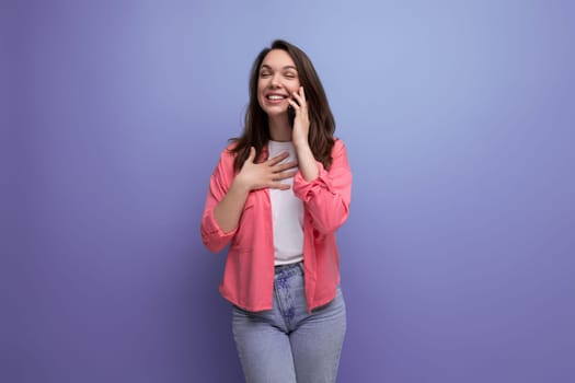 young woman in a pink shirt and jeans communicates on a mobile phone on a studio isolated background