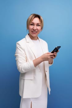 young blondie elegant female adult dressed in a jacket and dress holds a smartphone in her hands