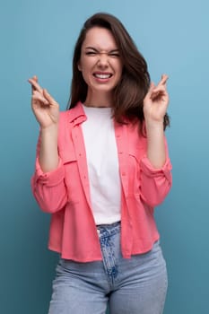 positive brunette lady with dark hair below her shoulders in a shirt and jeans crossed her fingers in anticipation of a surprise