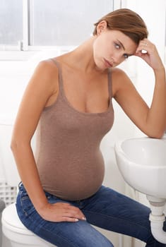 Nausea, pregnant woman and morning sickness in portrait, bathroom and uncomfortable person. Exhausted, moody and frustrated with illness, pregnancy and struggling with migraine pain on basin