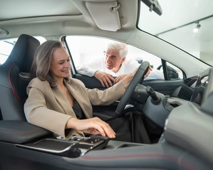 An elderly couple chooses a new car at a car dealership. Mature woman driving.
