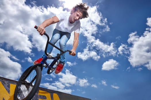 Bike, jump and teen on ramp for sport performance, ride or training for event at park with sky. Bicycle, stunt or kid balance on edge of board for cycling trick in competition or challenge with risk