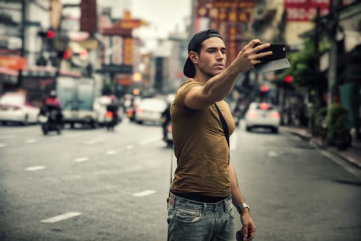 Photo of a man capturing a selfie amidst the vibrant hustle and bustle of a bustling city street in Thailand