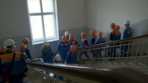 Workers on stairs. Clip. A lot of workers in hard hats are coming down stairs in building. Workers in large team walk up stairs in building