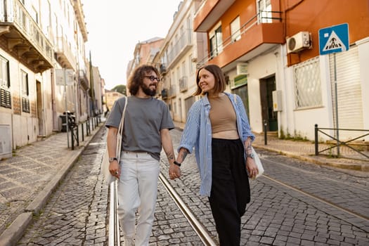 Smiling romantic hipster couple in love holding hands while walking on old city street