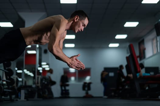 Muscular shirtless man doing push-ups in a jump in the gym.