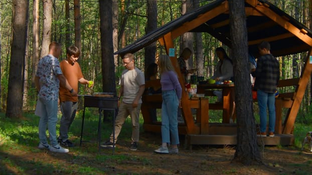 Friends in nature with gazebo. Stock footage. Friends relax in nature with barbecue in woods on sunny summer day. Outdoor recreation in gazebo with friends and barbecue