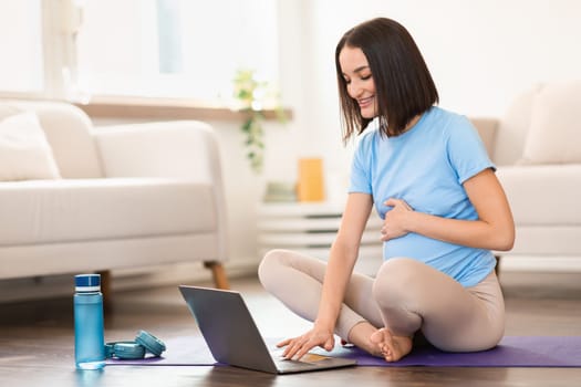 pregnant woman watching video workout lesson on laptop at home